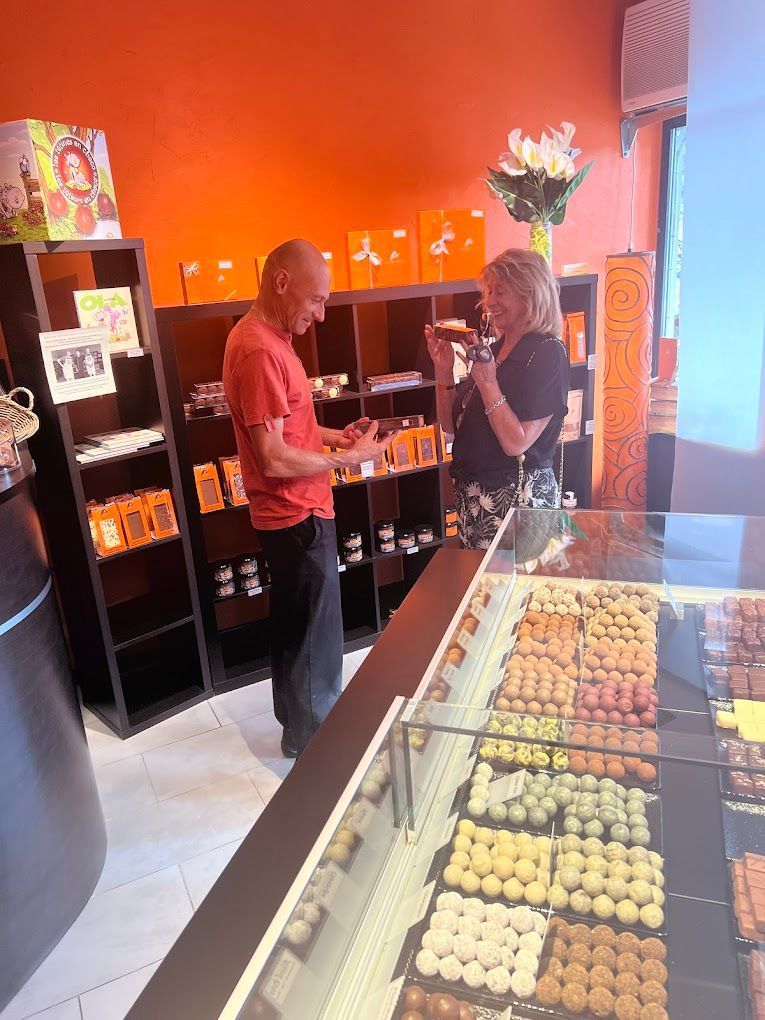 Un homme et une femme regardent des chocolats dans une boutique aux murs orange et à la vitrine remplie de friandises.