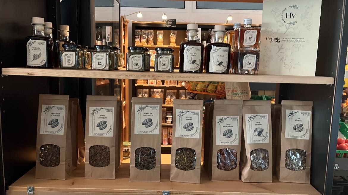 Présentoir en rayon de bocaux et de sacs en papier brun étiquetés, contenant probablement du thé et des épices, dans un magasin.