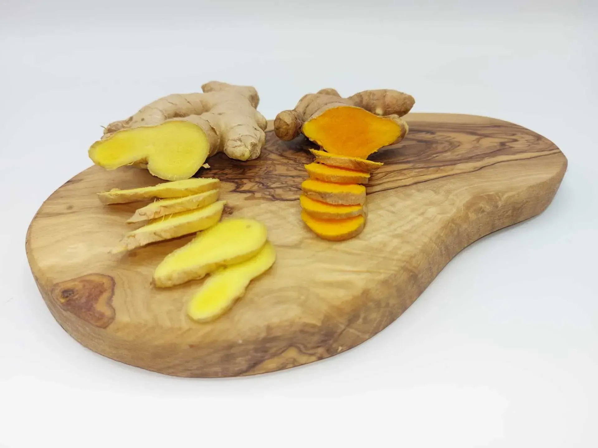 Gingembre et racine de curcuma tranchés sur une planche à découper en bois, sur fond blanc.