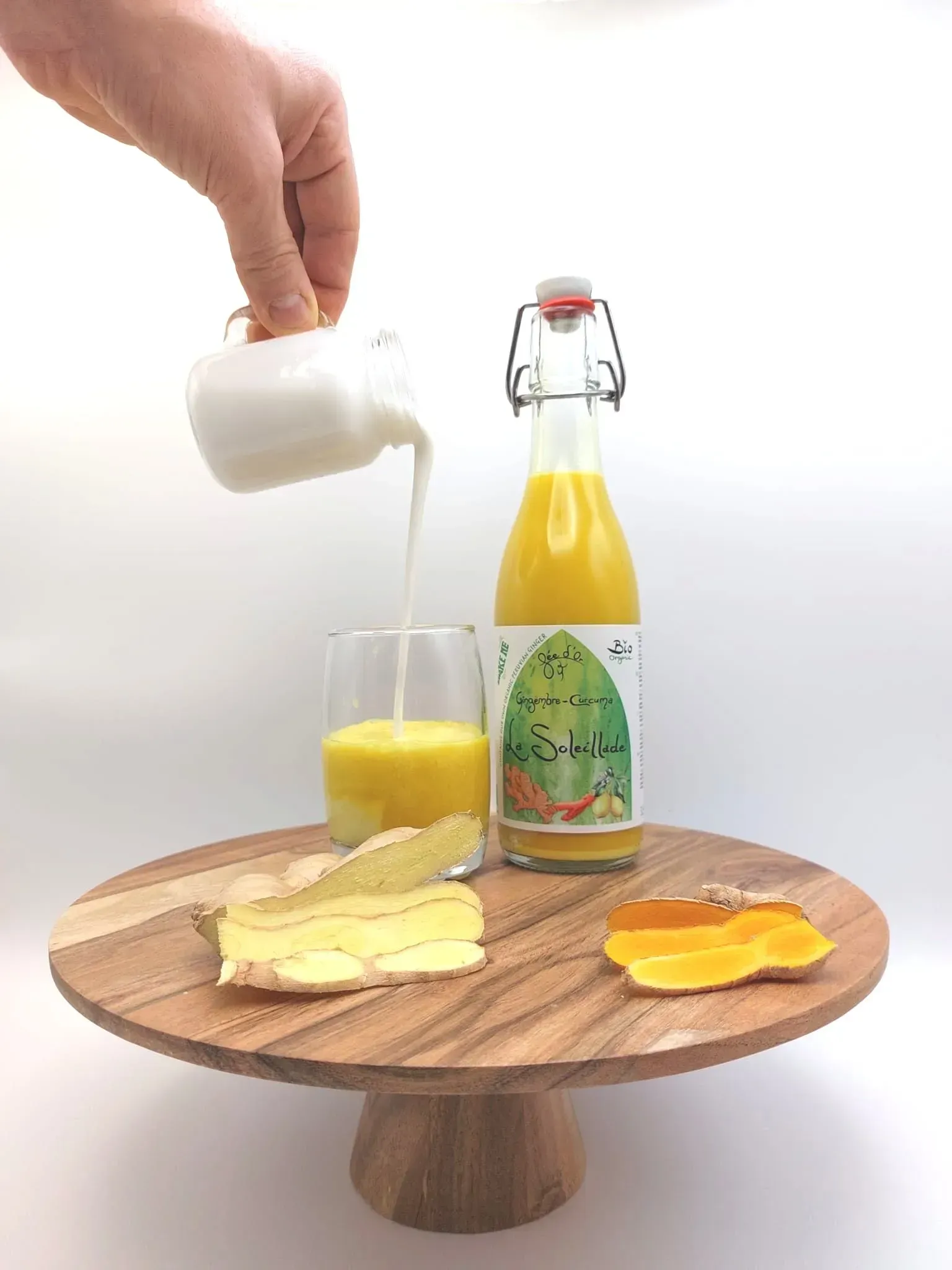 Crème versée à la main dans un verre de jus d'orange. Bouteille, fromage et fruits sur un plateau en bois.