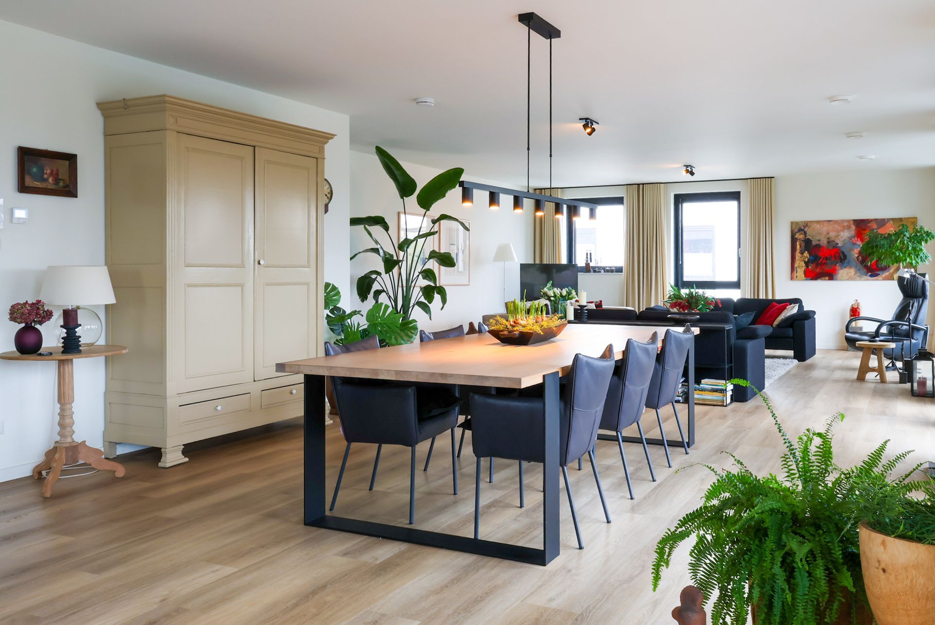 Ruime kamer met een lange houten eettafel, zwarte stoelen, een grote kast en prachtige kamerplanten in een modern penthouse.