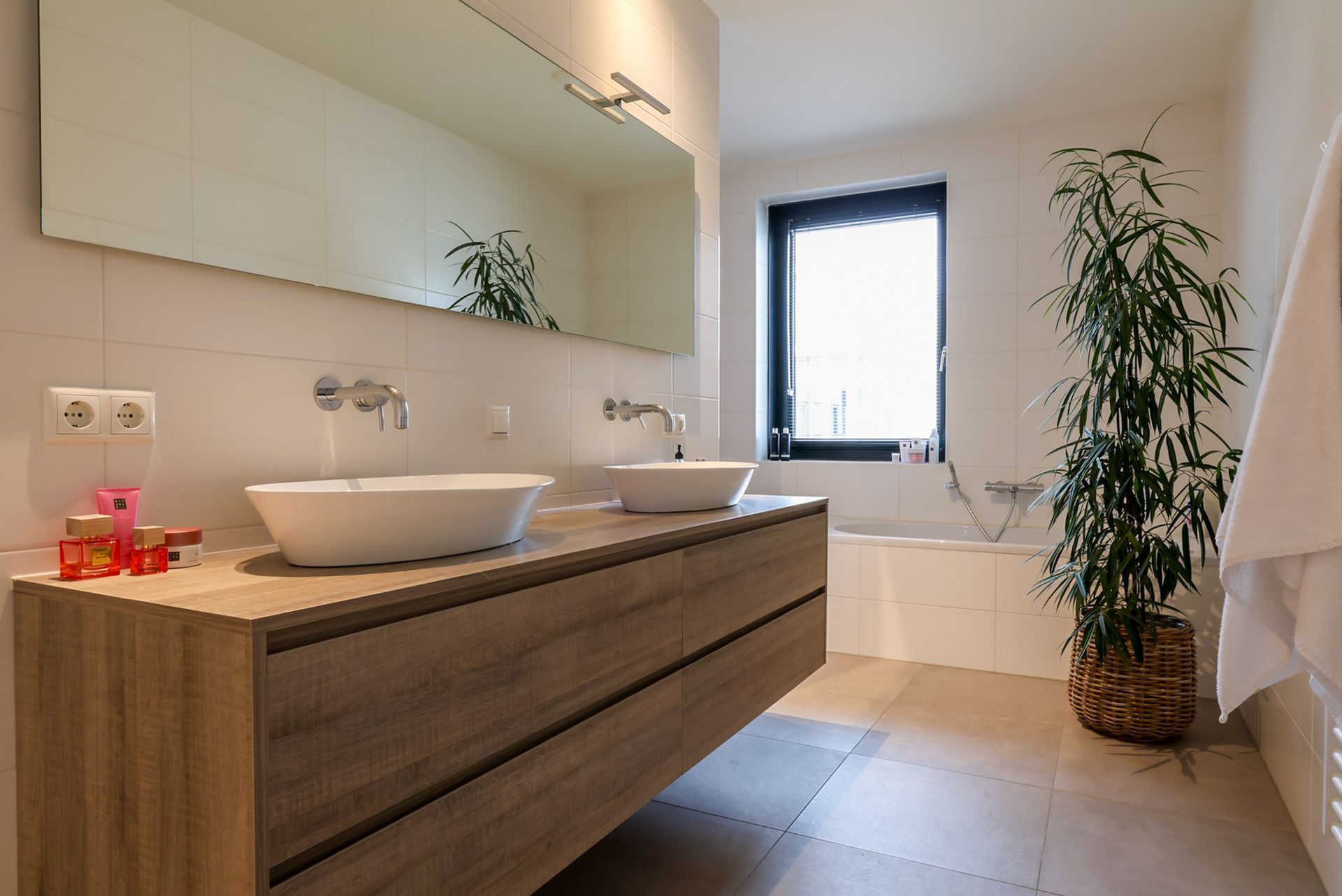 Moderne badkamer met een dubbele wastafel, een grote spiegel en een heerlijk ligbad. Achter de wastafel bevinden zich nog een royaal toilet en een ruime inloopdouche.
