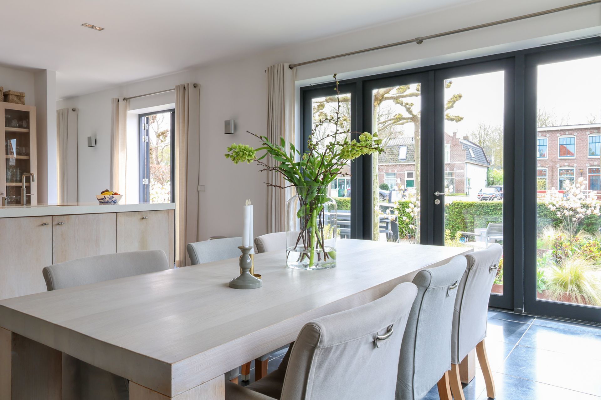 Een moderne woonkamer met maar liefst ruimte voor 3 royale banken. In beige en zwart, en een zwarte sofa, een houten salontafel, een hoogpolig vloerkleed en grote ramen van vloer tot plafond, die toegang geven tot het zeer grote balkon.