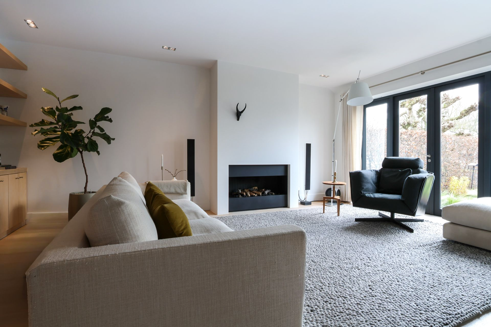 Een moderne woonkamer met maar liefst ruimte voor 3 royale banken. In beige en zwart, en een zwarte sofa, een houten salontafel, een hoogpolig vloerkleed en grote ramen van vloer tot plafond, die toegang geven tot het zeer grote balkon.