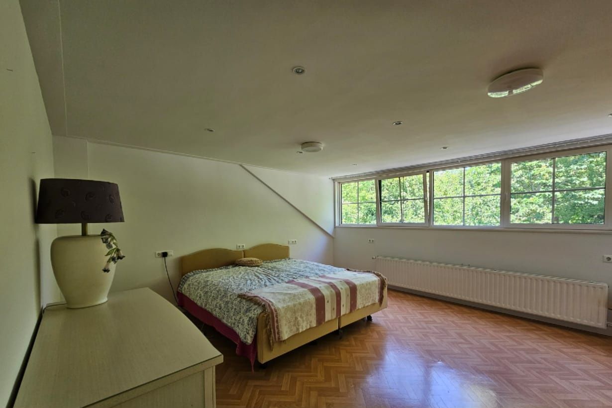 Slaapkamer vooraf gaand aan styling. Raampartijen zijn niet goed zichtbaar, looproutes naar het raam niet vrij. Bed, niet strak opgemaakt.