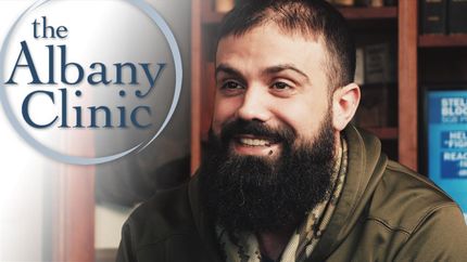 a man with a beard is smiling in front of a sign that says the albany clinic
