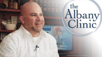 a bald man stands in front of a sign that says the albany clinic