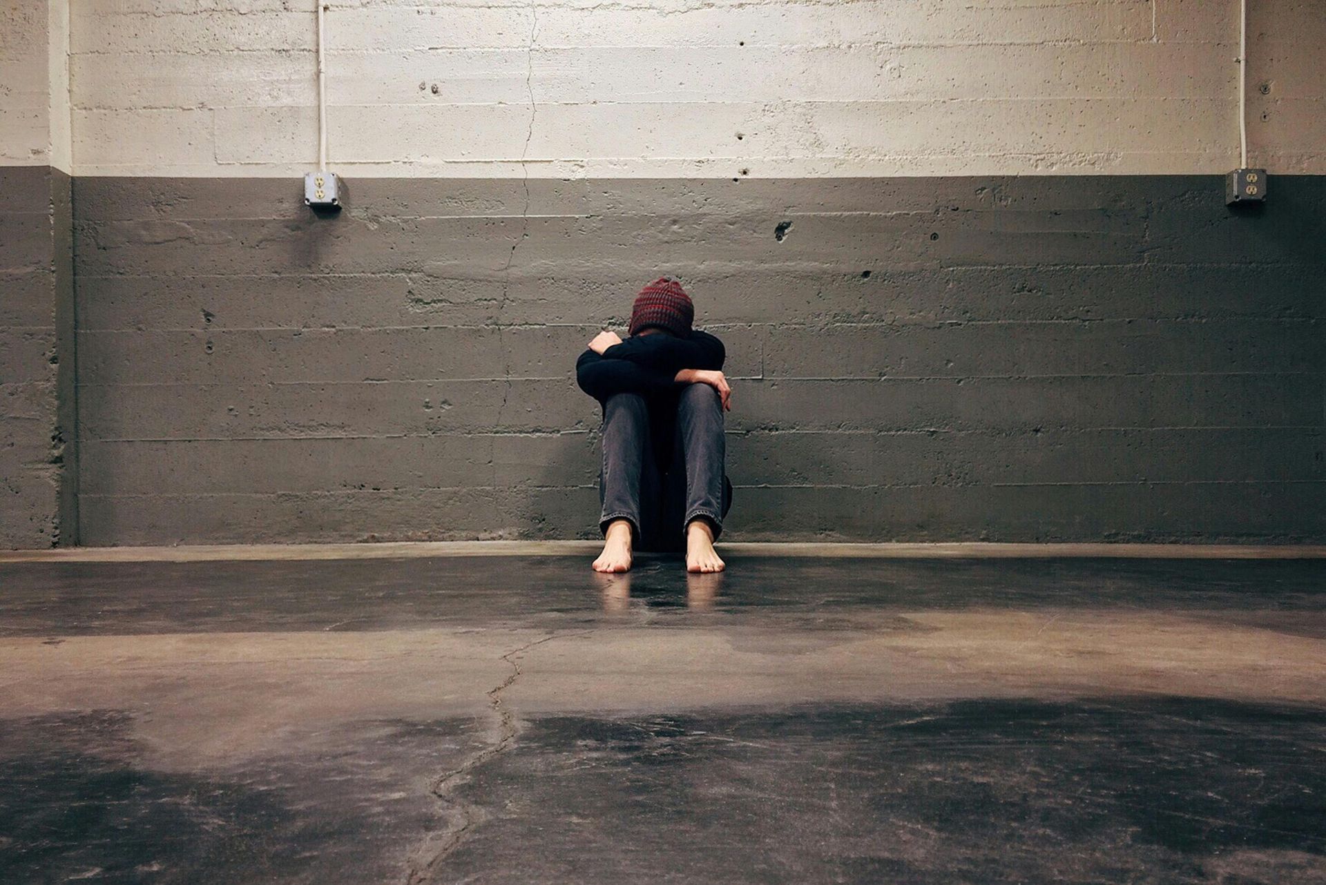 A person is sitting on the floor in front of a brick wall.