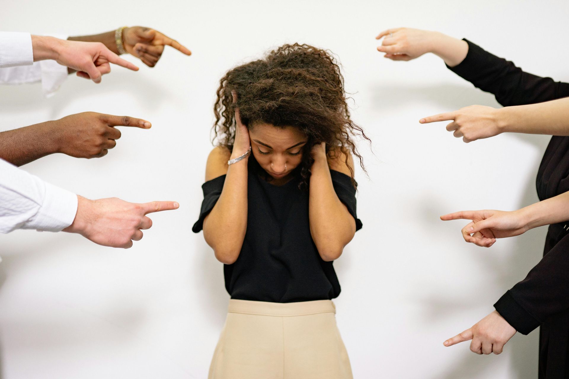 A woman is covering her ears while a group of people point at her.