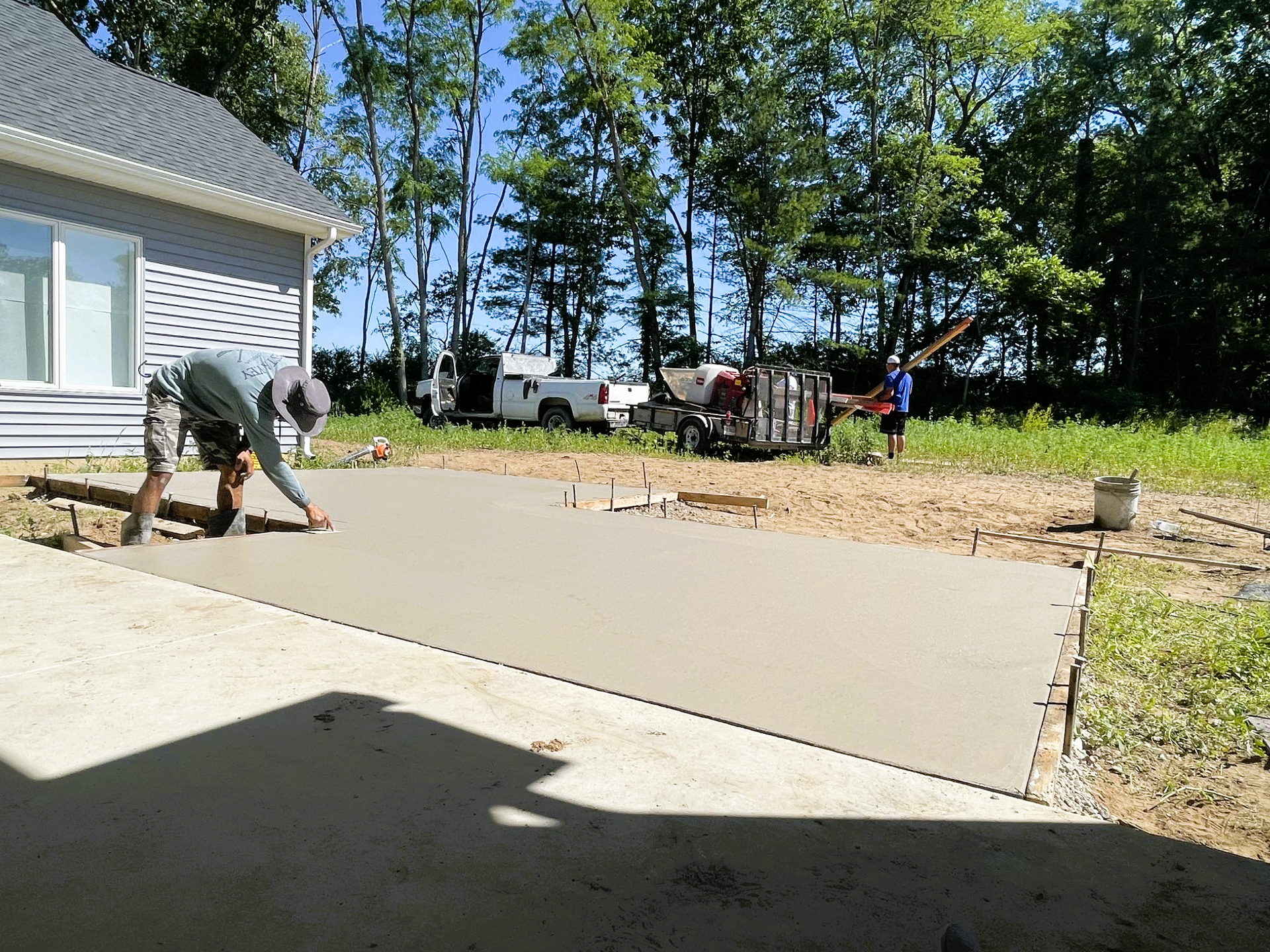 A man is working on a concrete driveway in front of a house.