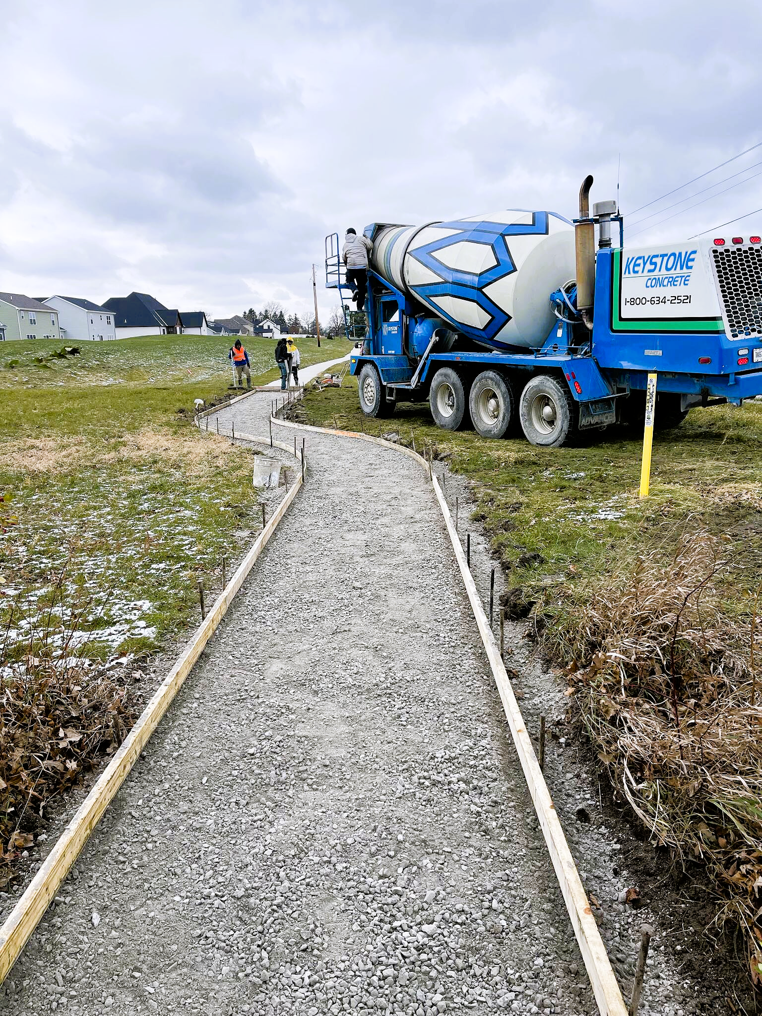 A concrete mixer truck is driving down a gravel path.