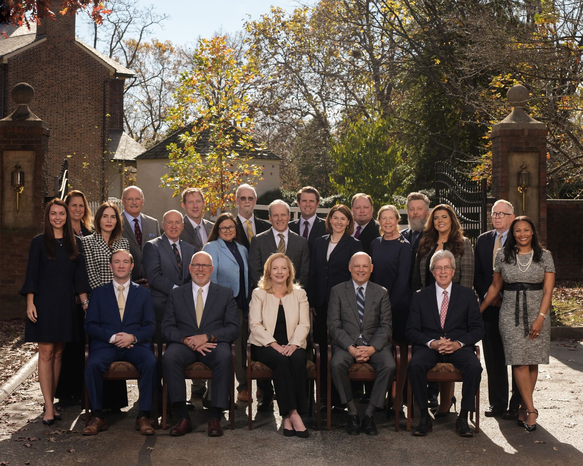 Group portrait of individuals in business attire posed outdoors in front of a brick building and gate.