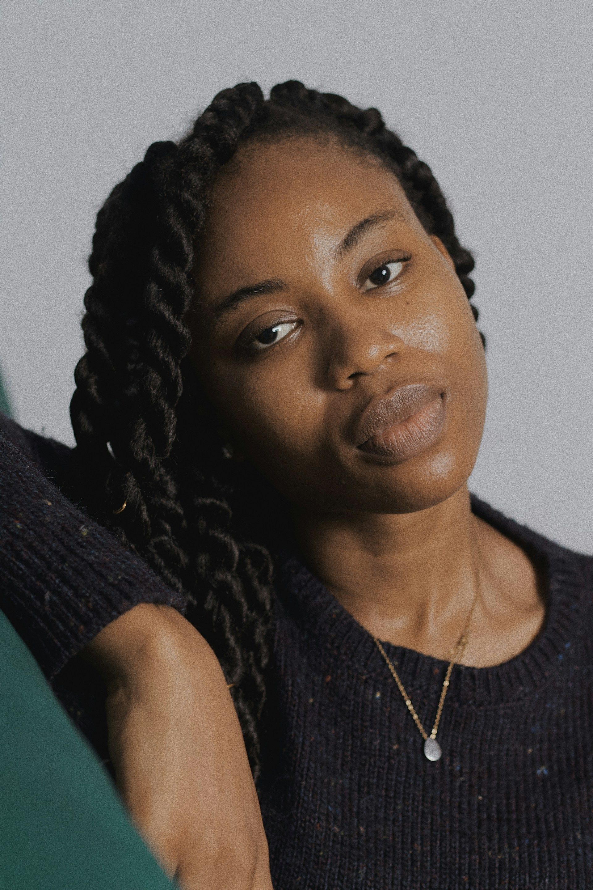 Woman with dark skin and twisted black hair, wearing a dark sweater, looking at the camera.
