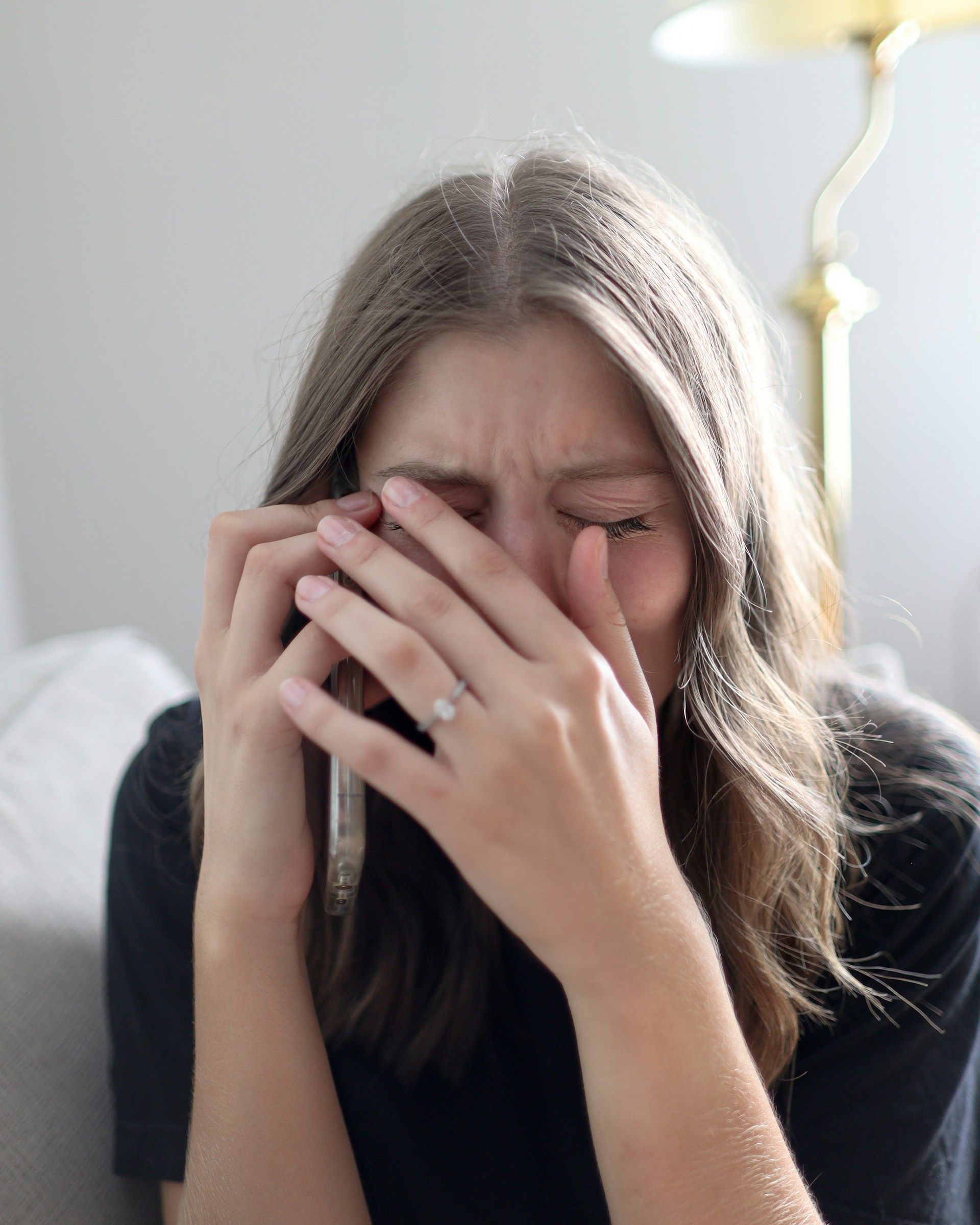Woman with hands covering her face, appearing distressed, holding a phone.