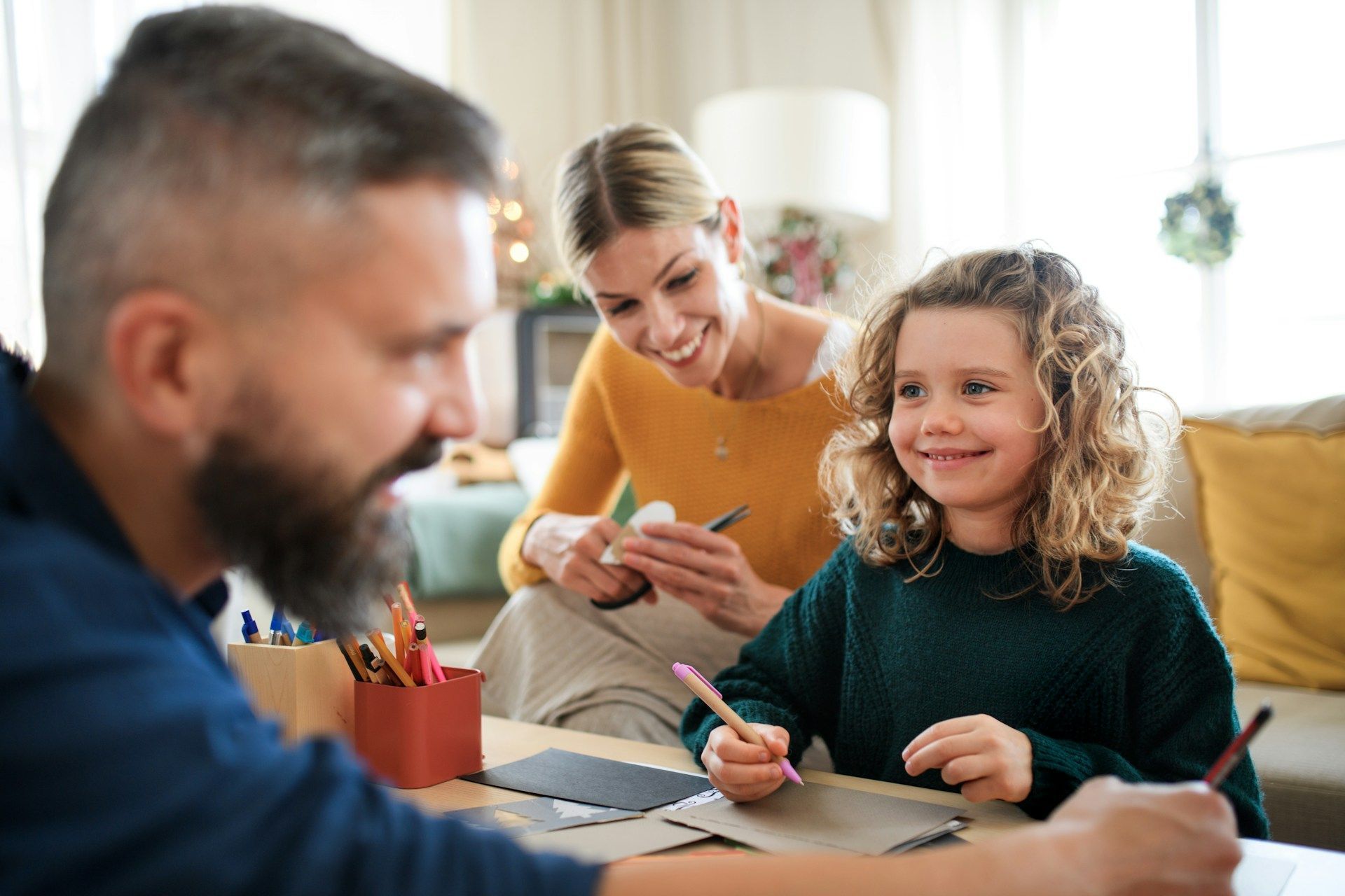 Family, father, mother, and child, crafting at home. Smiling, colorful pencils, living room.