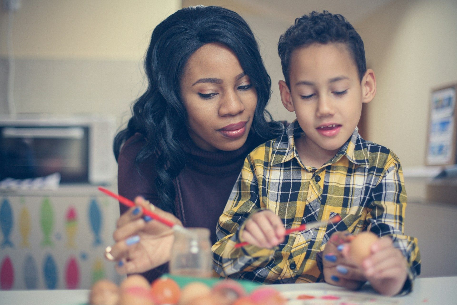 Woman and child painting Easter eggs together in a kitchen setting.