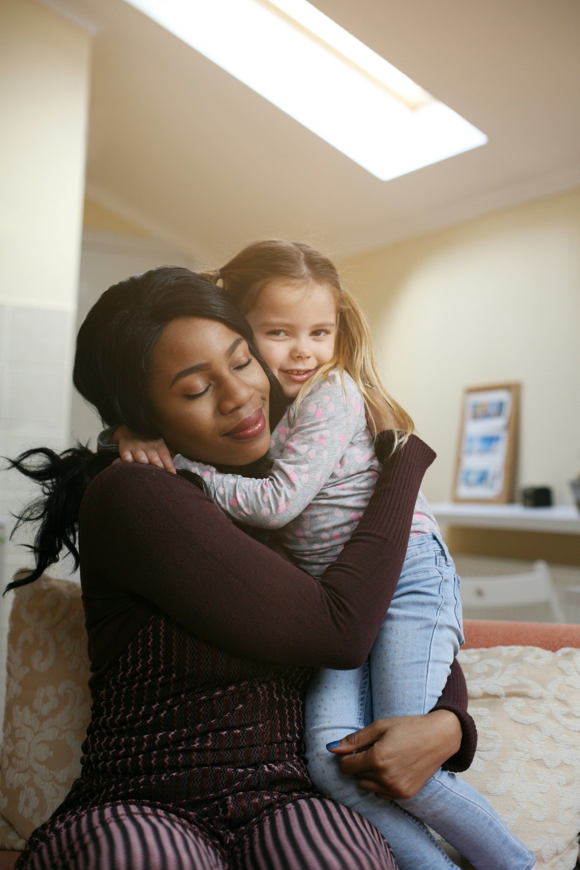 Woman embraces a young girl indoors. They are smiling.