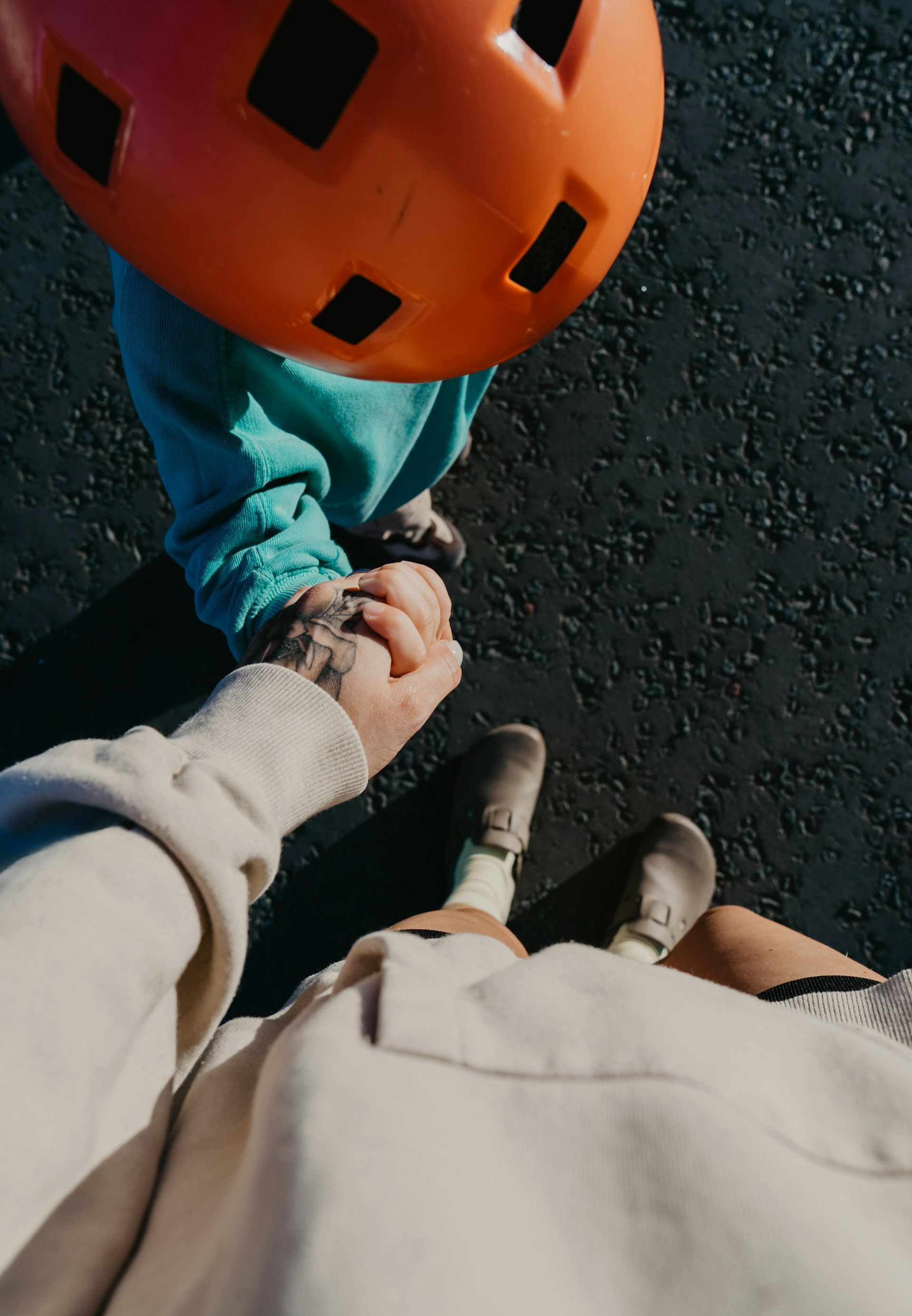 Person holds a child's hand. The child wears a blue outfit and orange helmet.