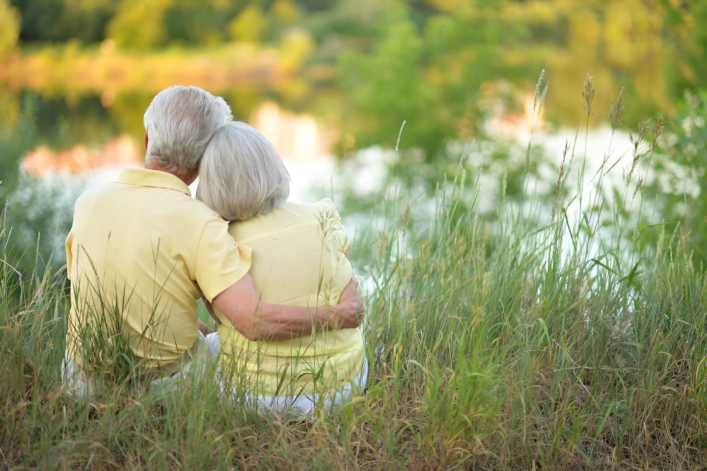 An Elderly Couple is Sitting in the Grass Hugging Each Other — Active Lifestyle Supports In Shellharbour, NSW
