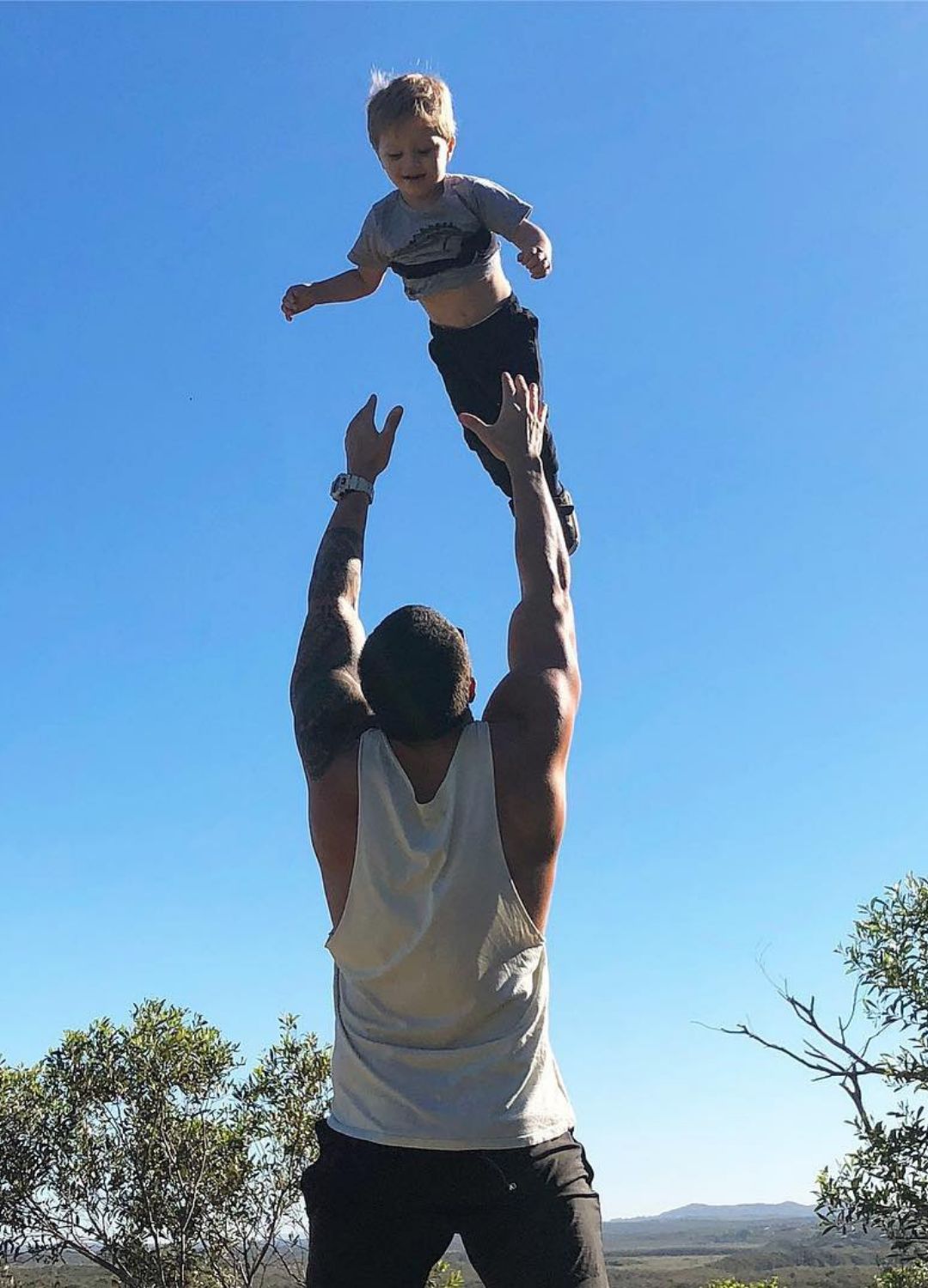 Man throwing a child up in the air against a clear blue sky.
