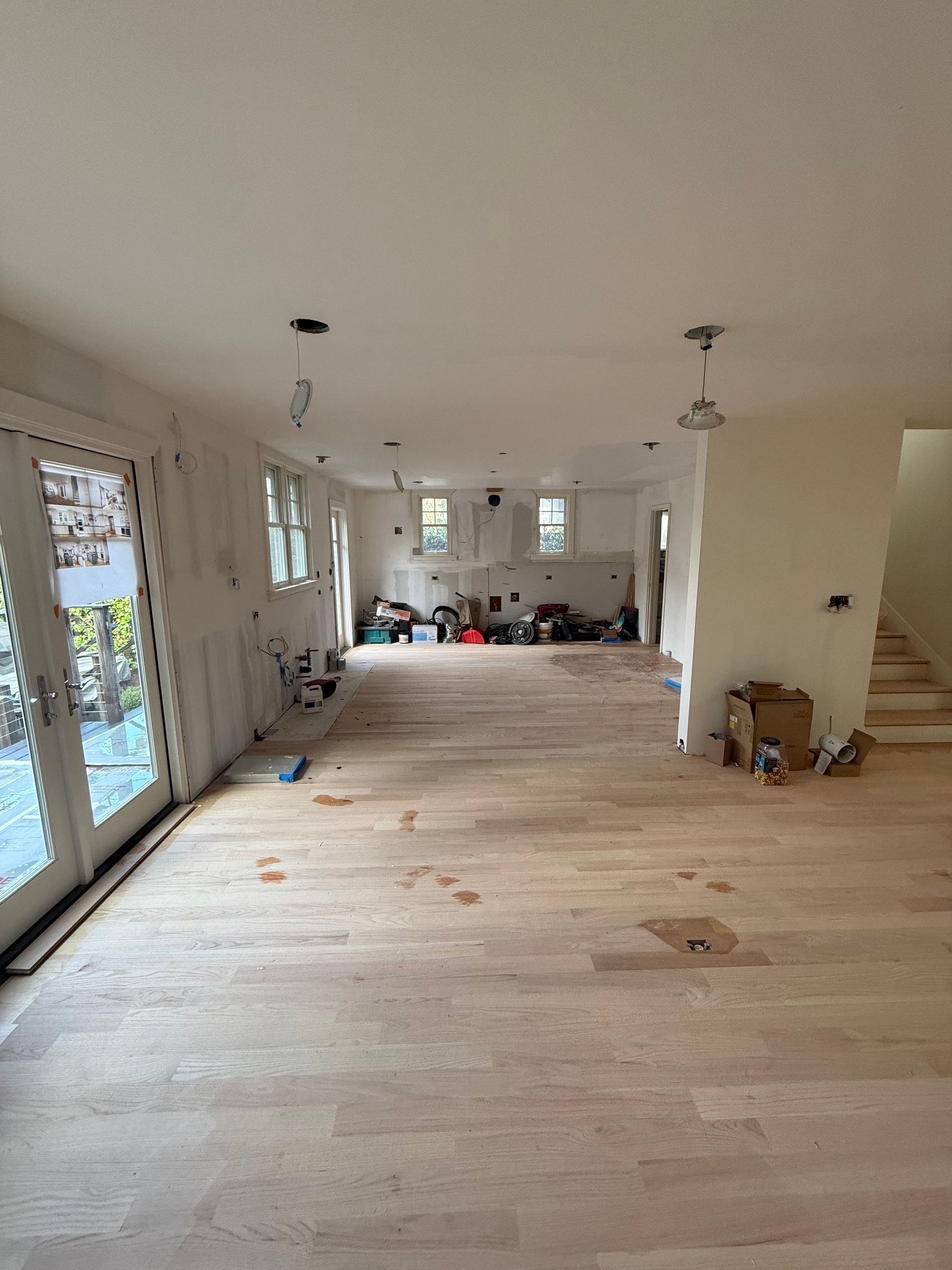 A room under renovation with wooden ceiling beams, drywall patches, ladders, and scaffolding on a hardwood floor.