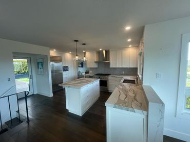 A modern kitchen featuring white cabinets, a matching central island, stone countertops, and dark wood floors.