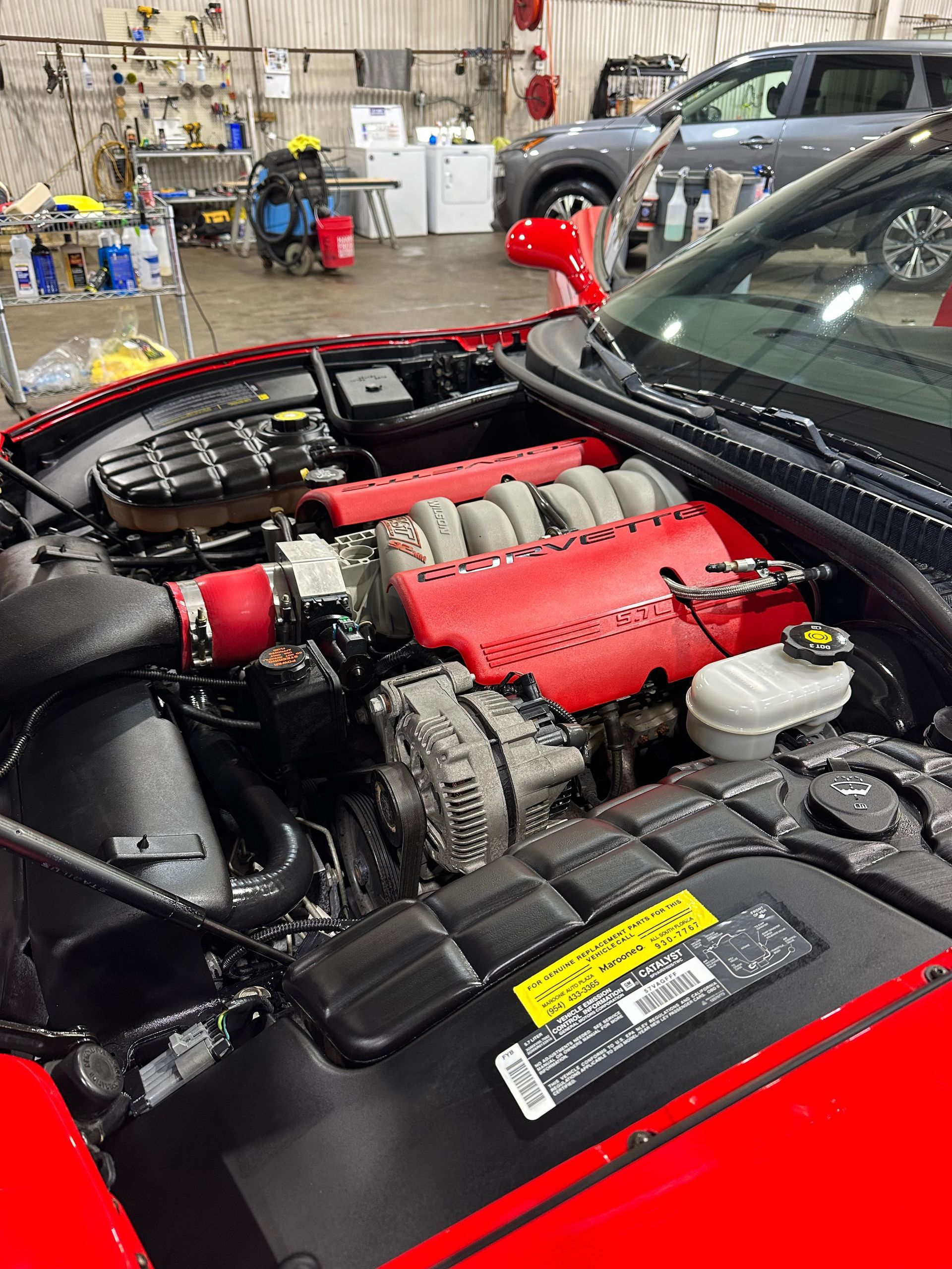 Red car engine bay with exposed engine and red intake components in a workshop￼