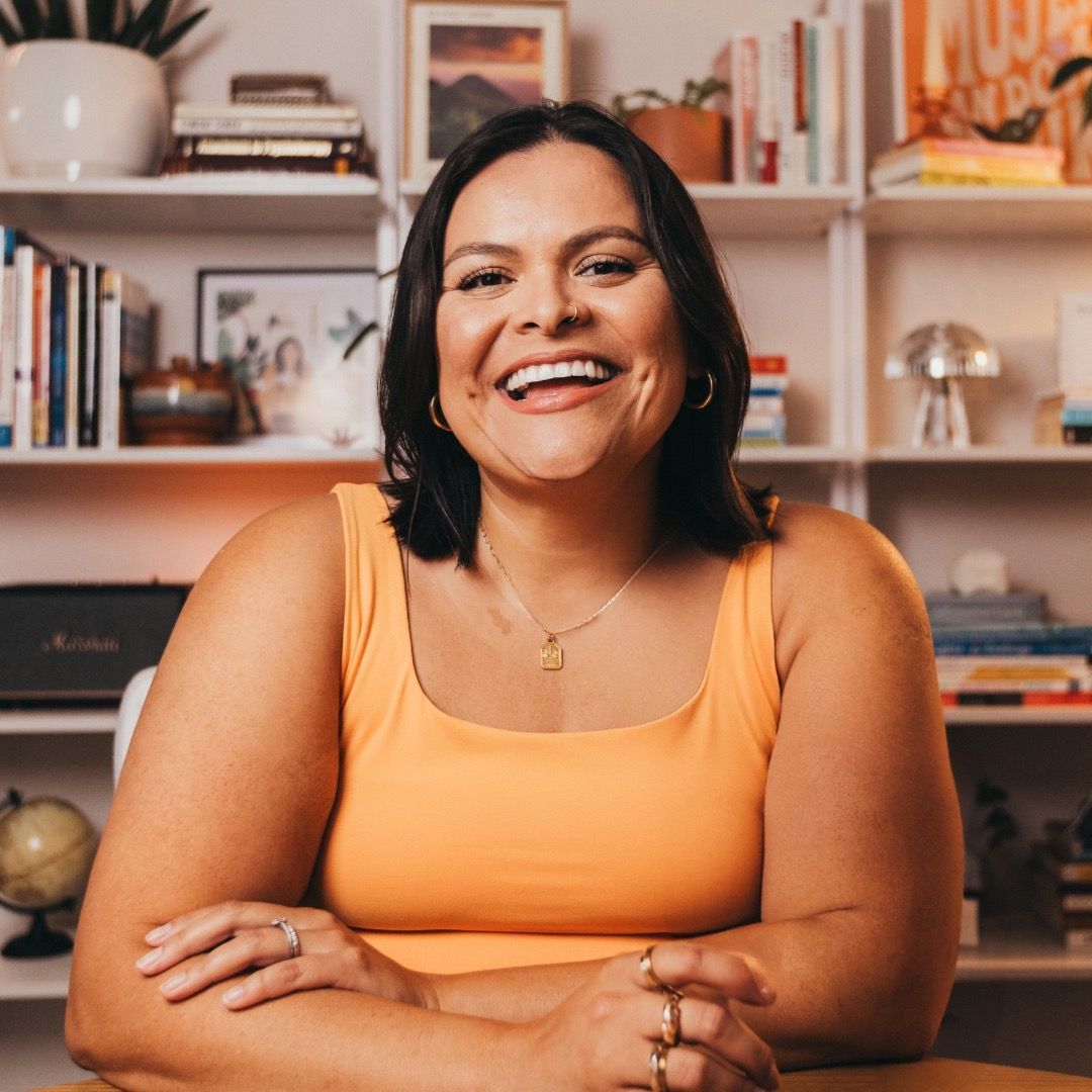 A woman in a pink shirt is smiling in front of a bush.