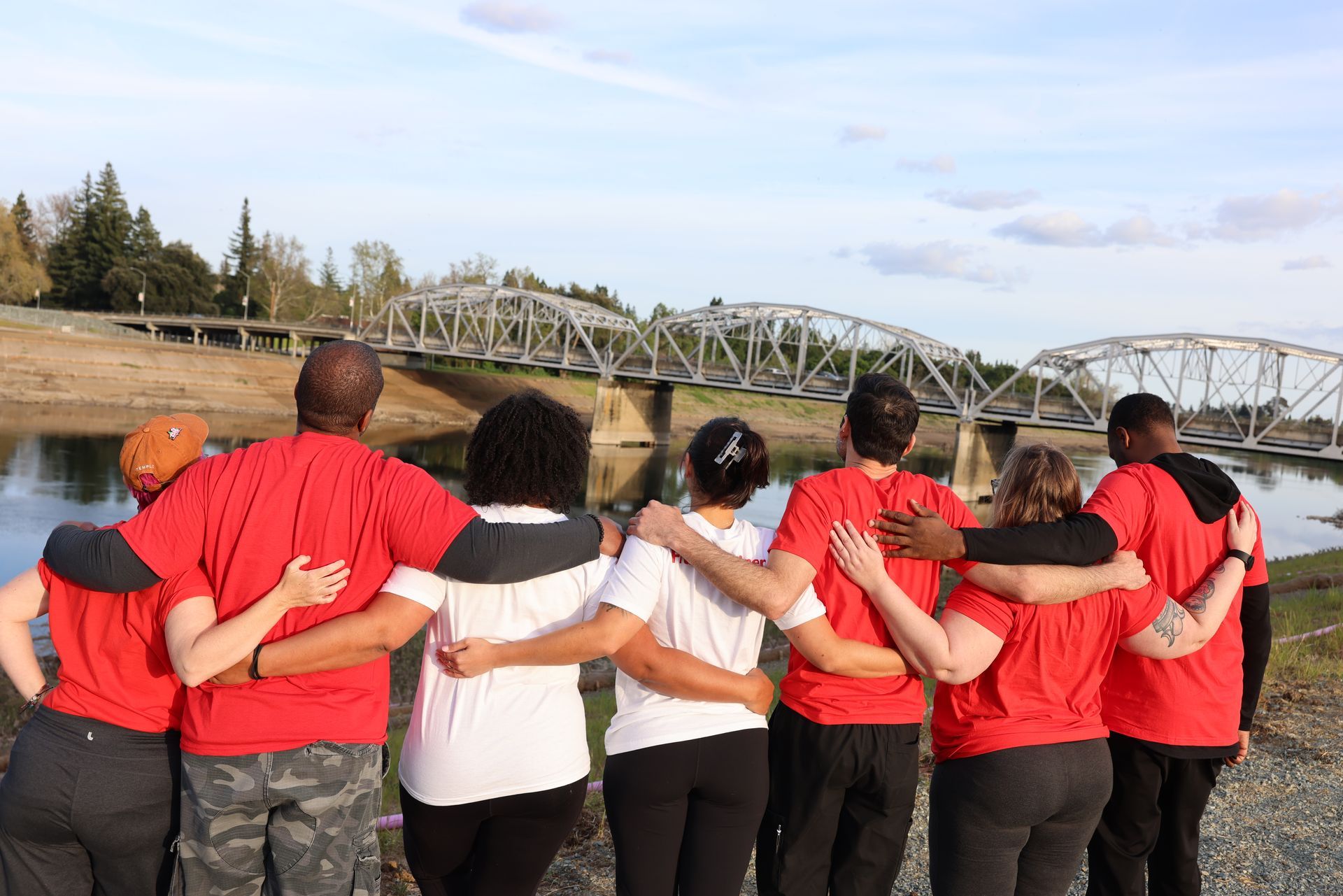 A group of people are hugging each other in front of a bridge.