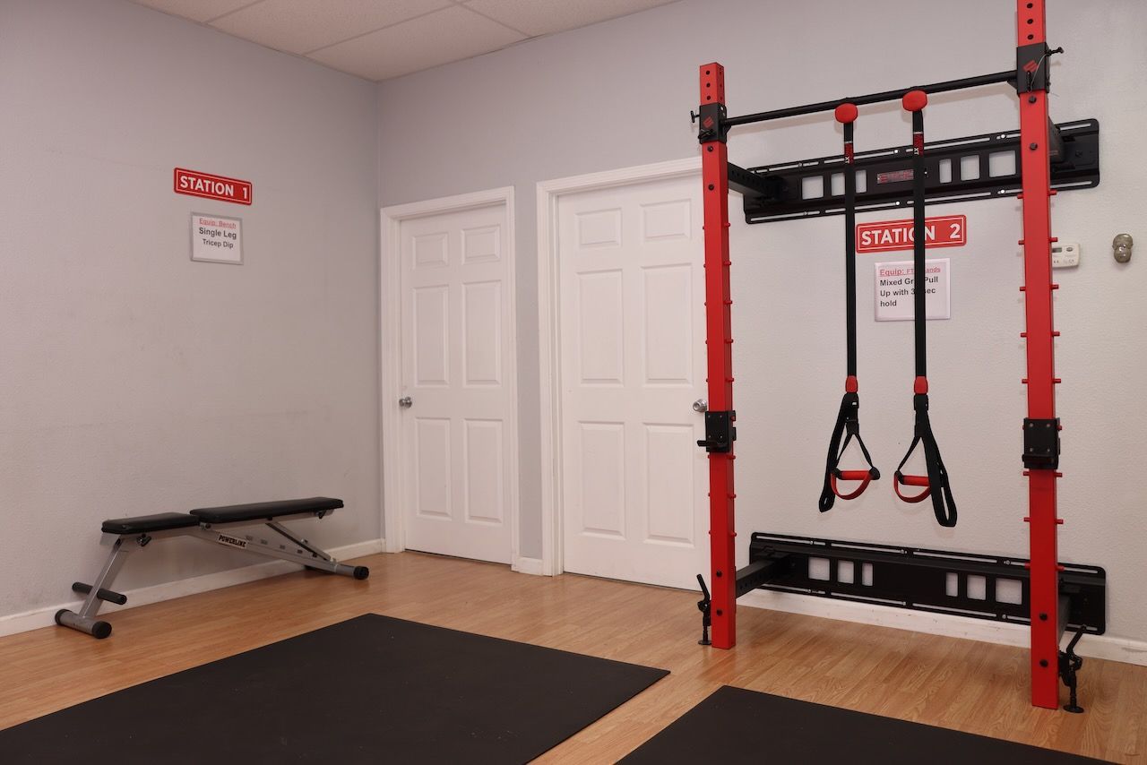 A gym with a bench , a mat , and a trx machine.