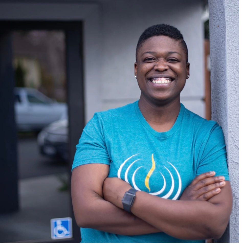 A woman in a red shirt is smiling in front of a brick wall