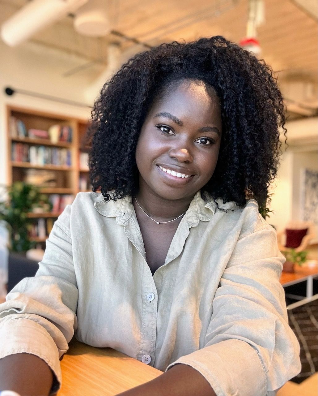 A woman with curly hair is sitting at a table and smiling for the camera.