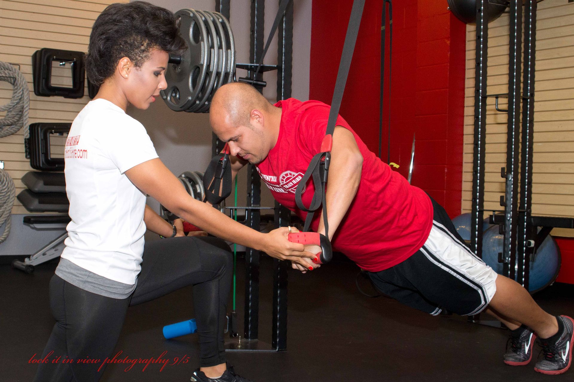 A woman is helping a man do push ups in a gym