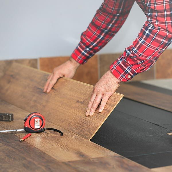 A man in a plaid shirt is measuring a piece of wood.