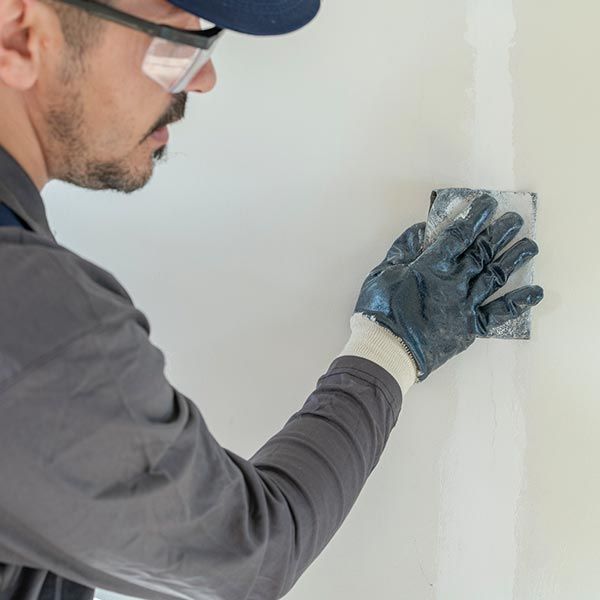 A man wearing safety glasses and gloves is plastering a wall.