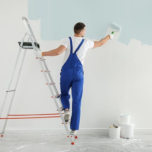 A man is standing on a ladder painting a wall.