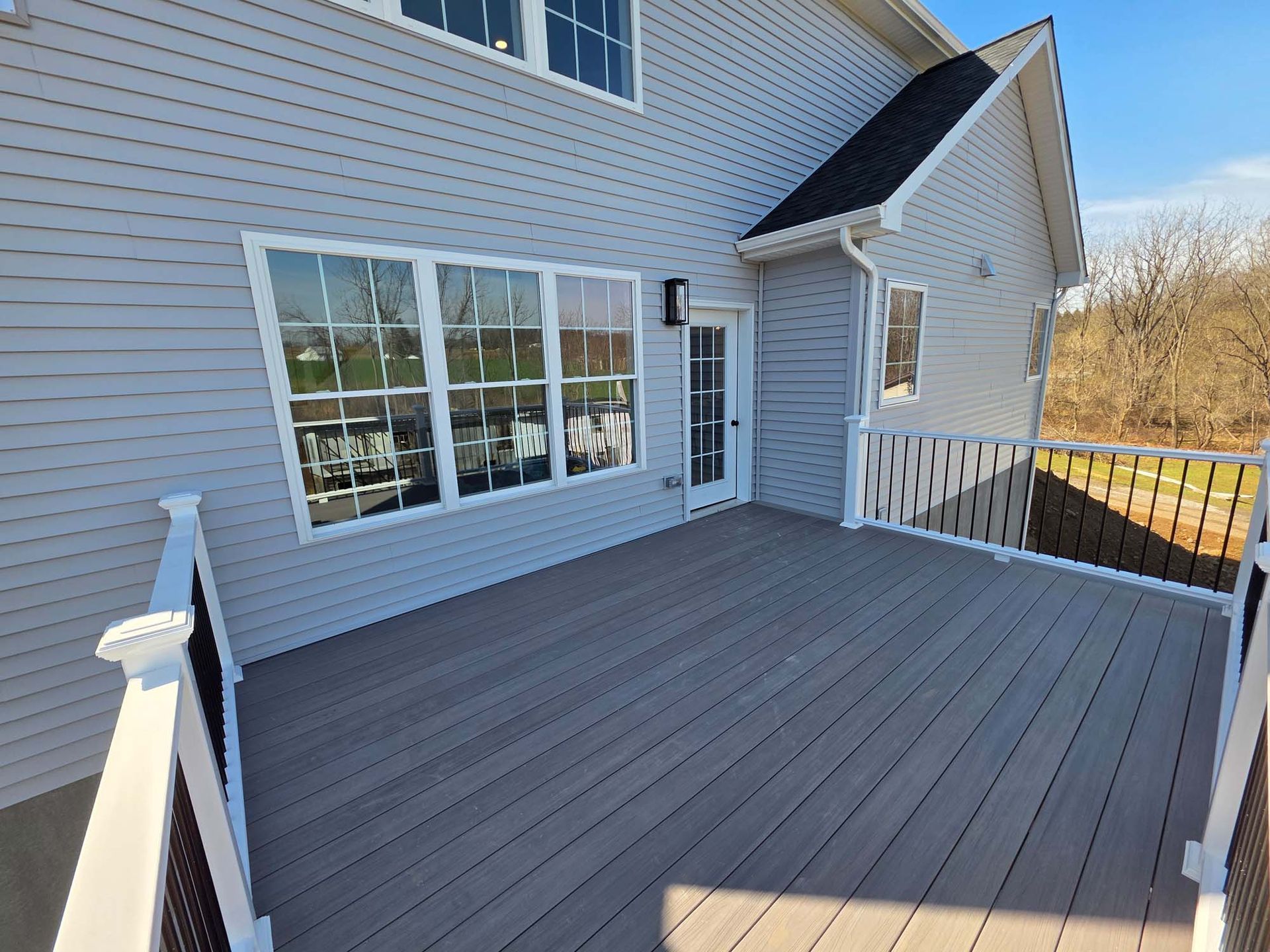 A large deck with a white railing is in front of a house.