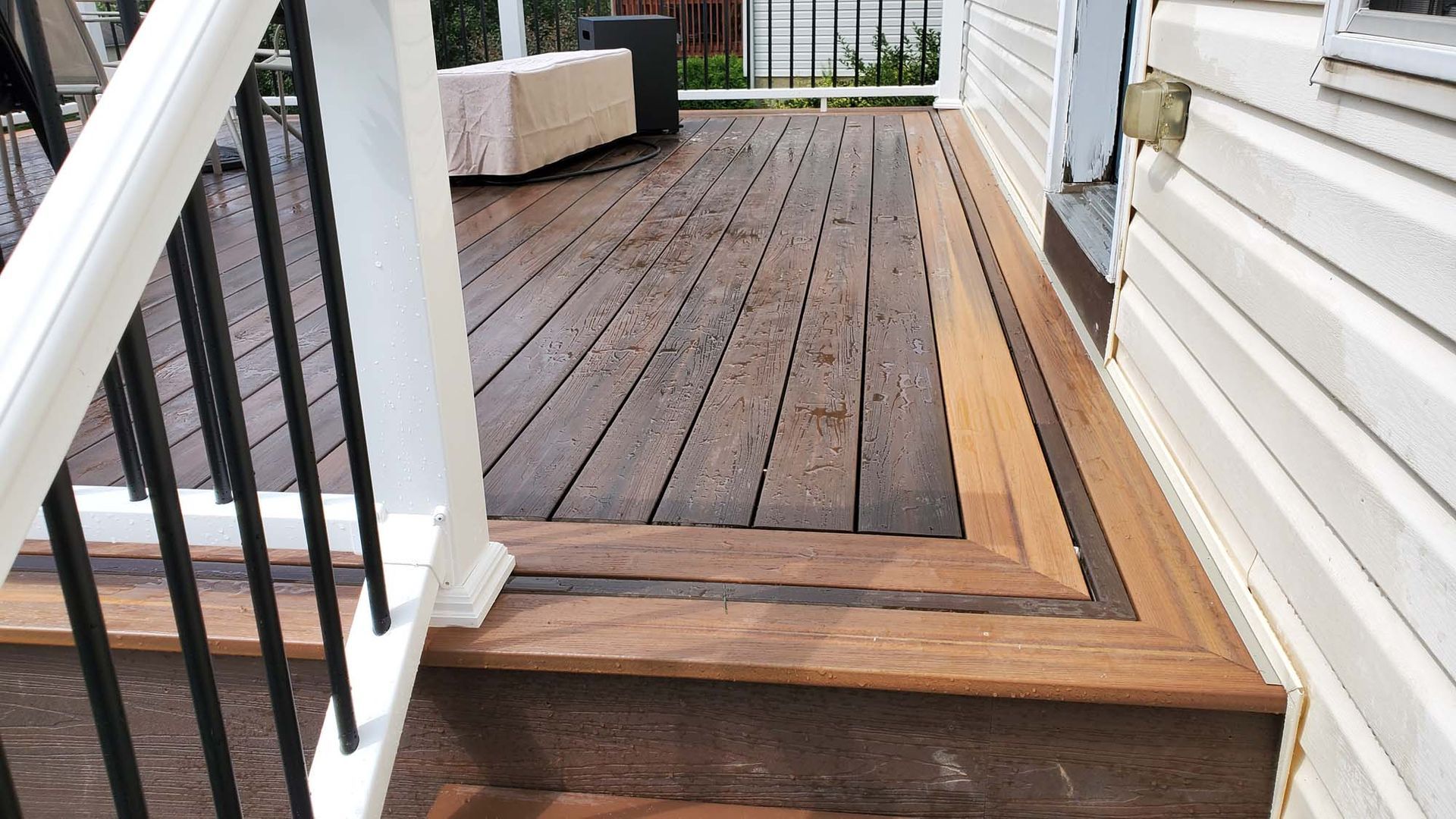 A wooden deck with stairs leading up to it next to a white house.