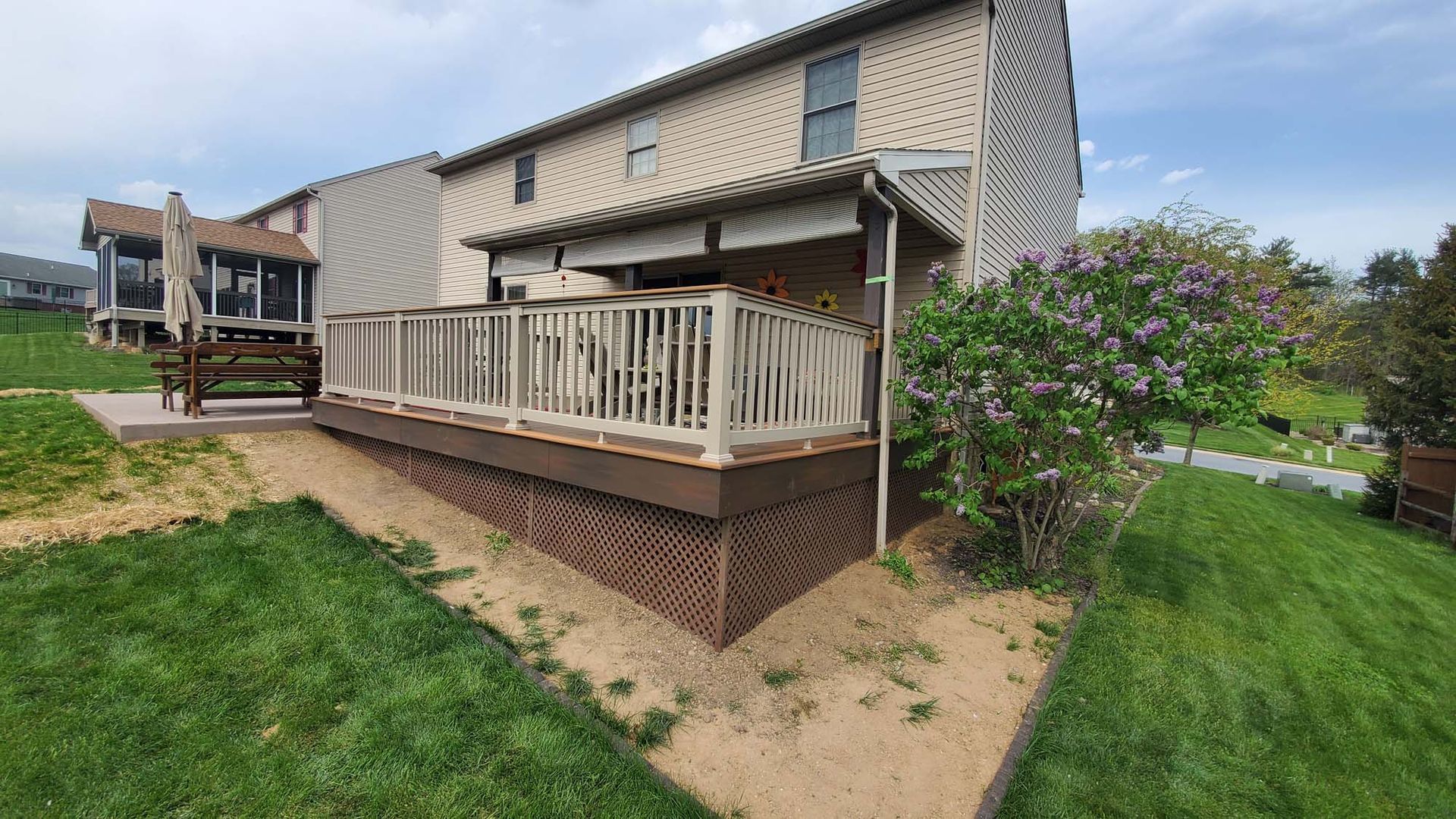 A large deck with a white railing is in the backyard of a house.