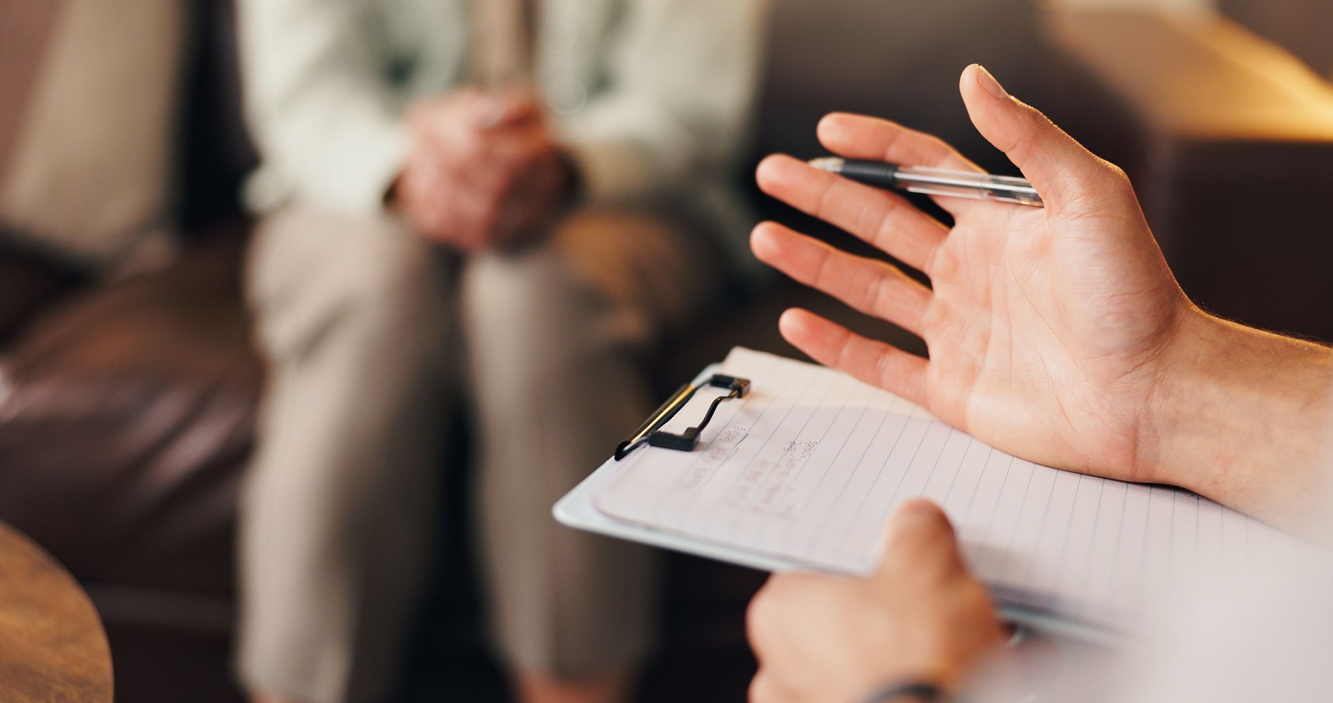 a close-up of a hand holding a pen and clipboard with notes, engaged in a conversation with a person