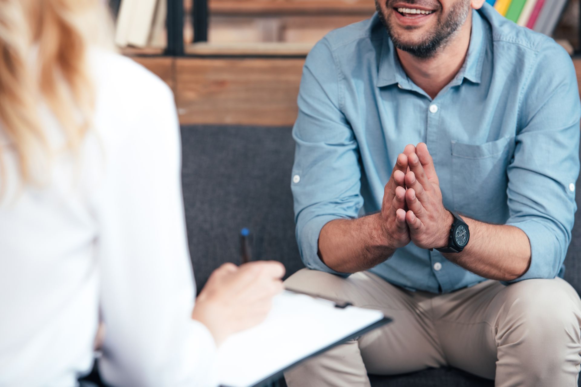 Female counselor writing in clipboard and smiling male holding hand palms together during therapy.