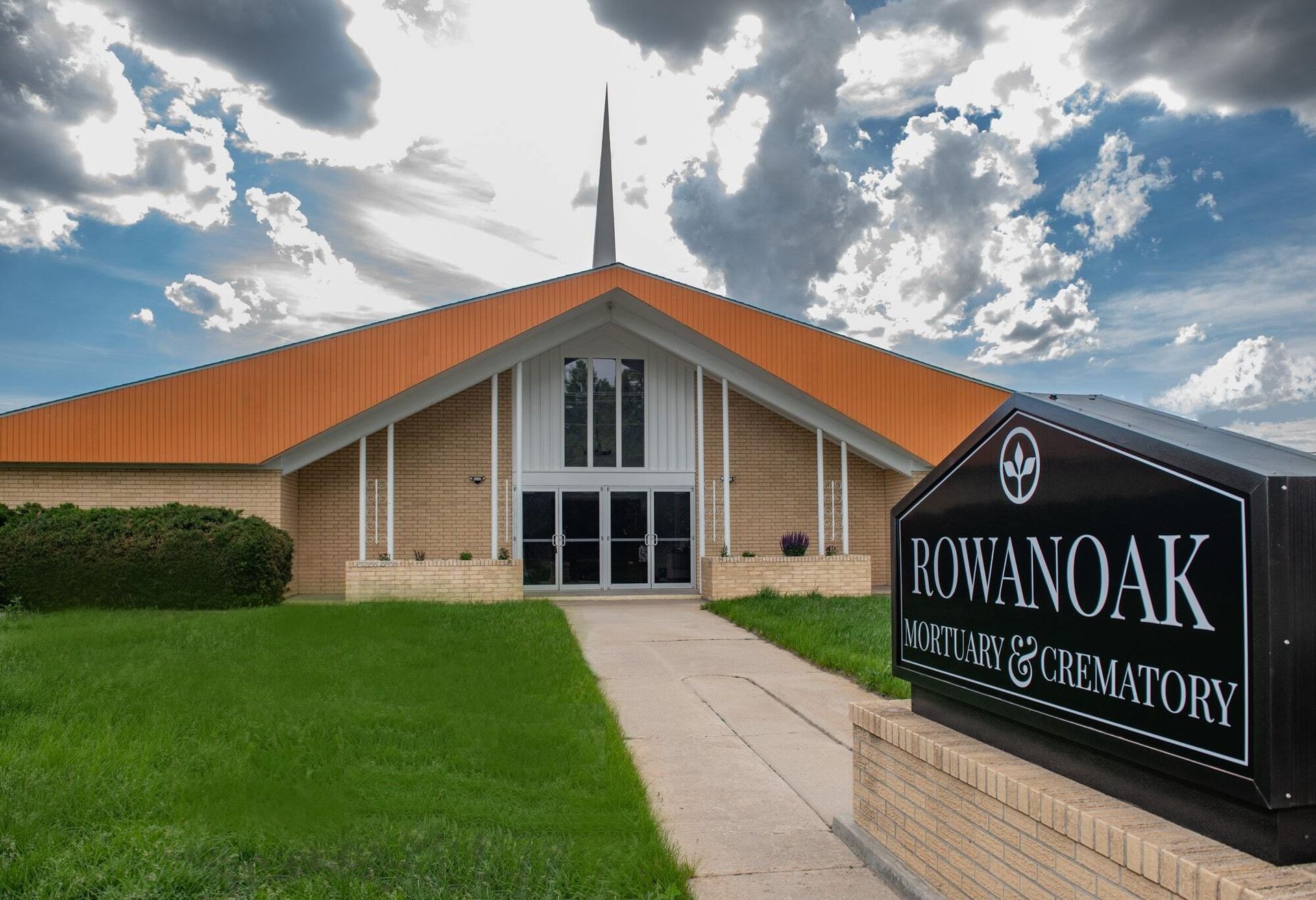 Rowanoak Mortuary & Crematory building with sign, pathway, and cloudy sky.