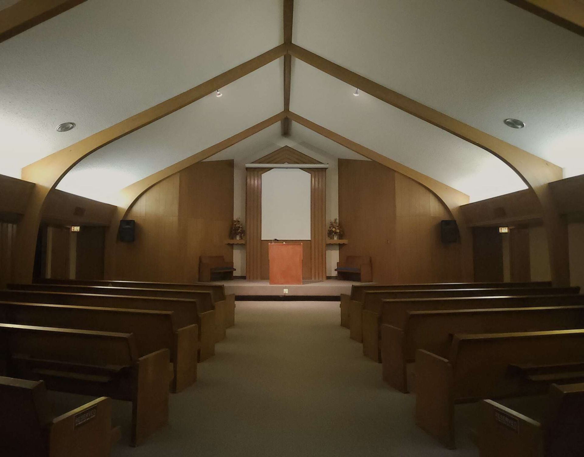 Interior of a chapel with rows of wooden pews facing a wooden altar and a white wall backdrop.