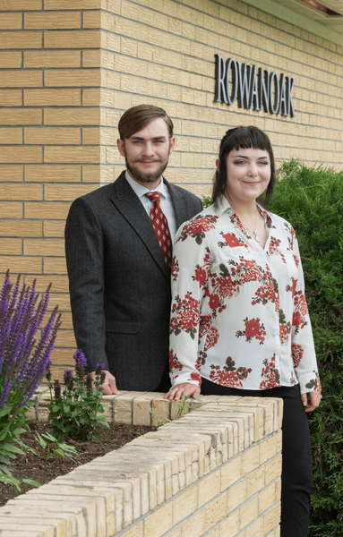 Man in suit and woman in floral top stand by a brick building,