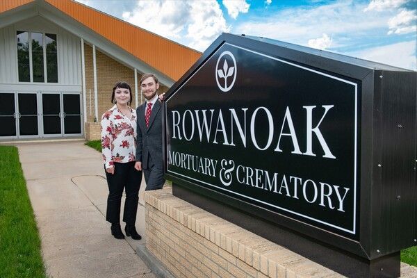 Two people standing near a sign for Rowan Oak Mortuary & Crematory; exterior shot of the building.