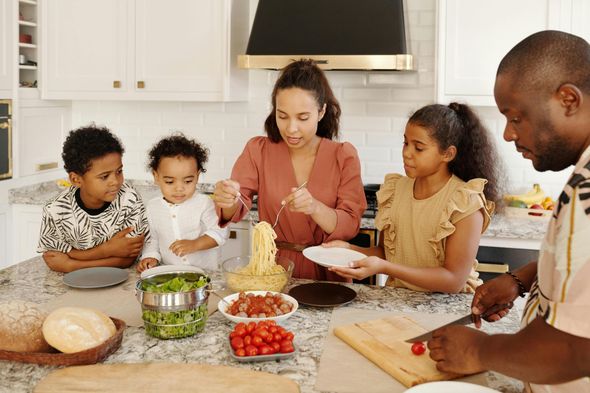 A family preparing a meal together in a bright kitchen, with pasta, salad, and fresh ingredients on the granite island.