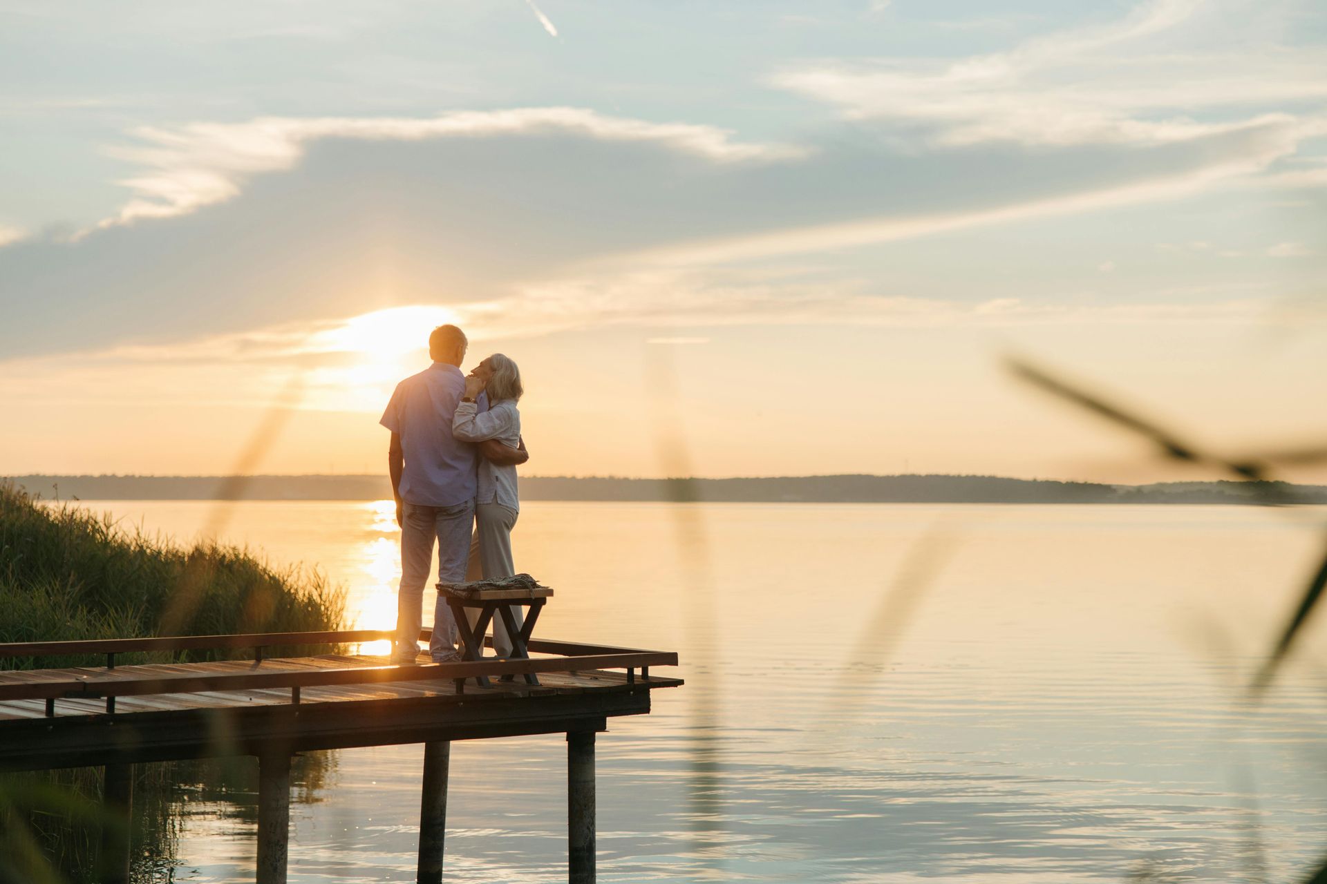 A man and a woman are standing on a pier overlooking a lake at sunset.