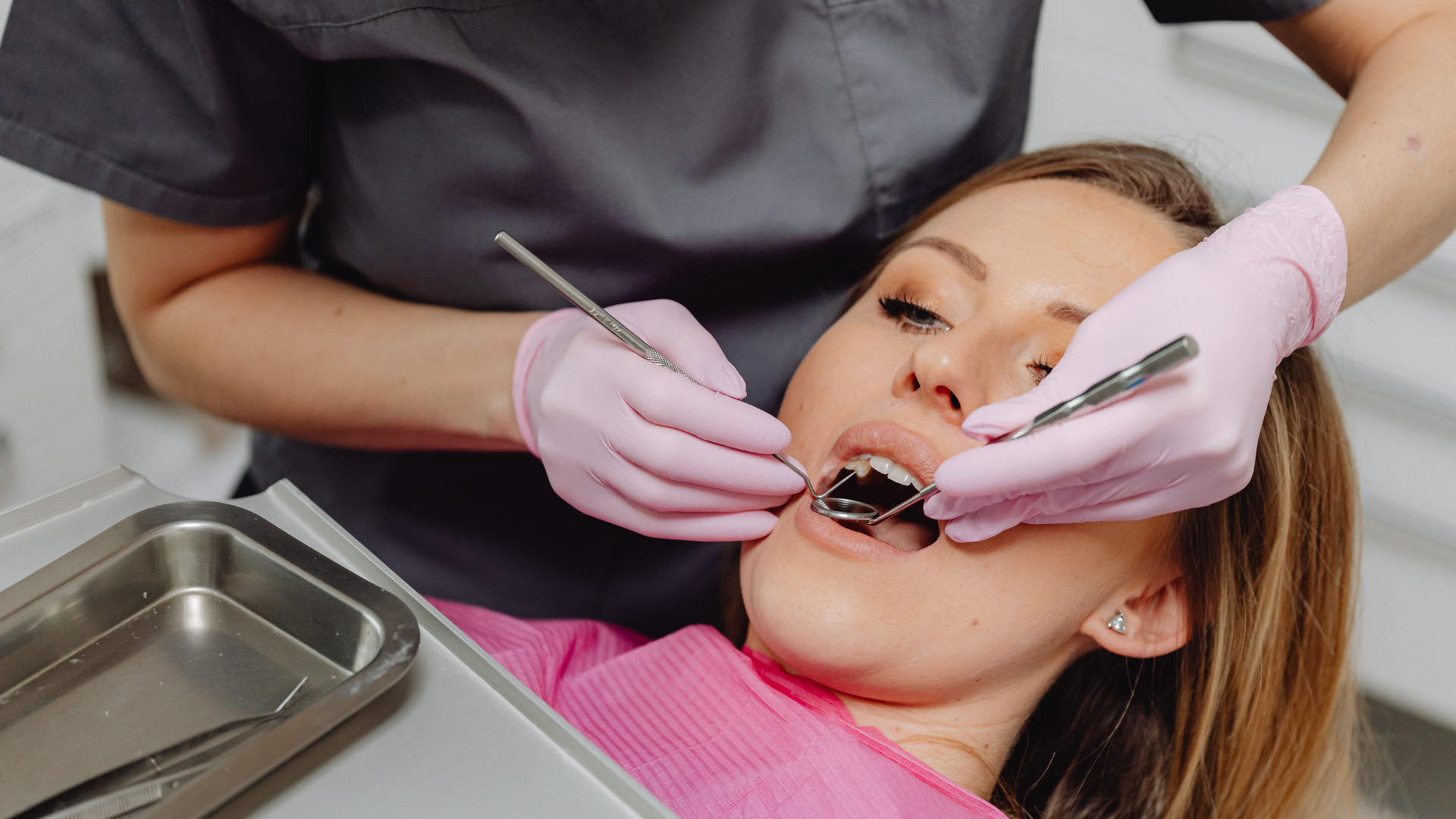 Dentist examining a patient's teeth with a mirror and probe. The patient is in a dental chair.