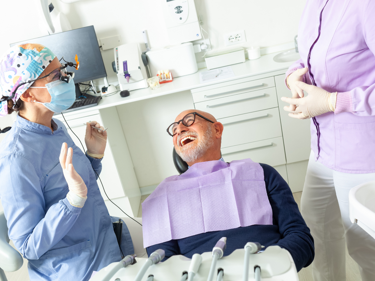 Dentist and assistant in dental office with a laughing patient in chair.