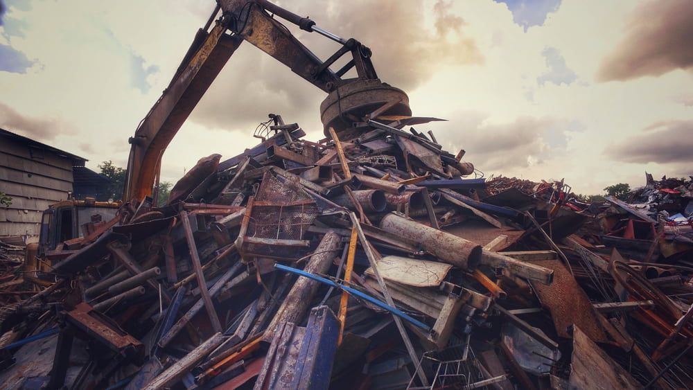 Excavator Claw Lifting Scrap Metal in a Junkyard Under a Cloudy Sky — Central Scrap Metal in Toowoomba, QLD